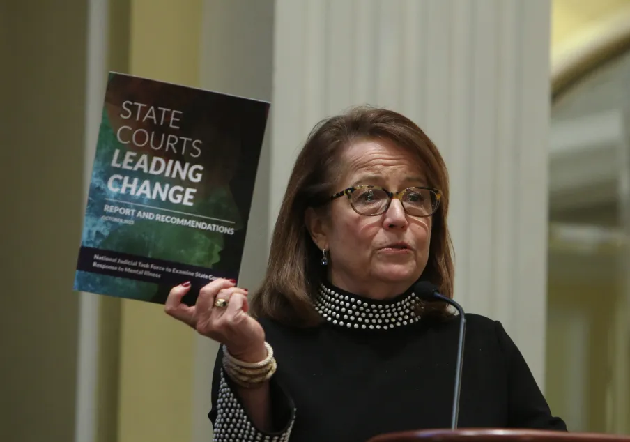 Woman holding "State Courts Leading Change" report at podium